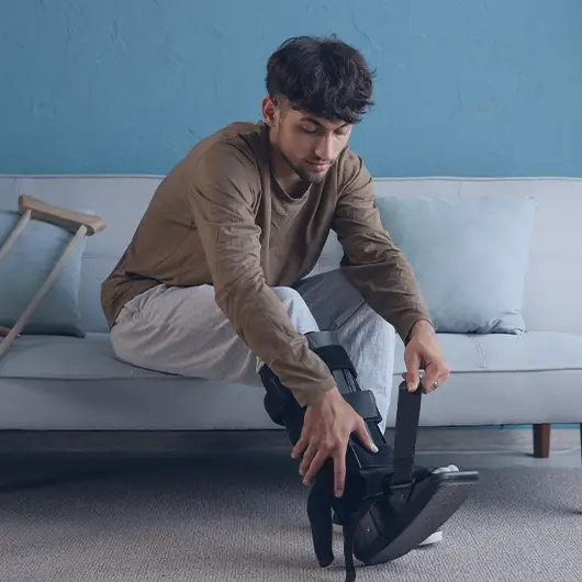 Injured man with sprained ankle and black splint orthosis sitting on the sofa