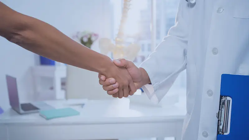 New patient shaking Dr hand, Dr holding clipboard with patient information
