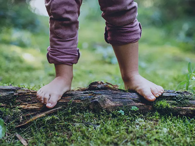 Barefoot kid standing on top of a long in the path