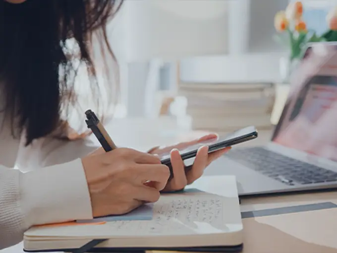 Person looking at a phone and writing notes in a notebook